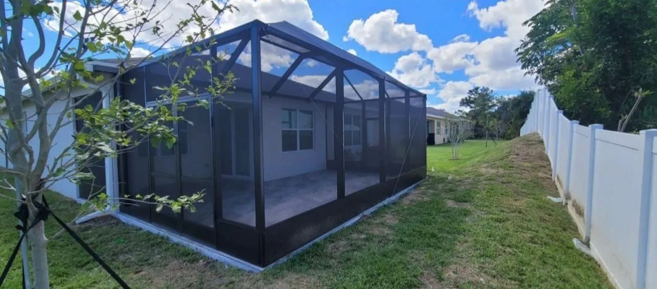 Screened patio in a backyard with white fence and blue sky.