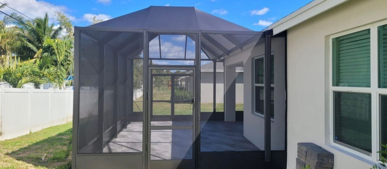Screened-in porch attached to a light-colored house. Blue sky. Green grass and trees visible.
