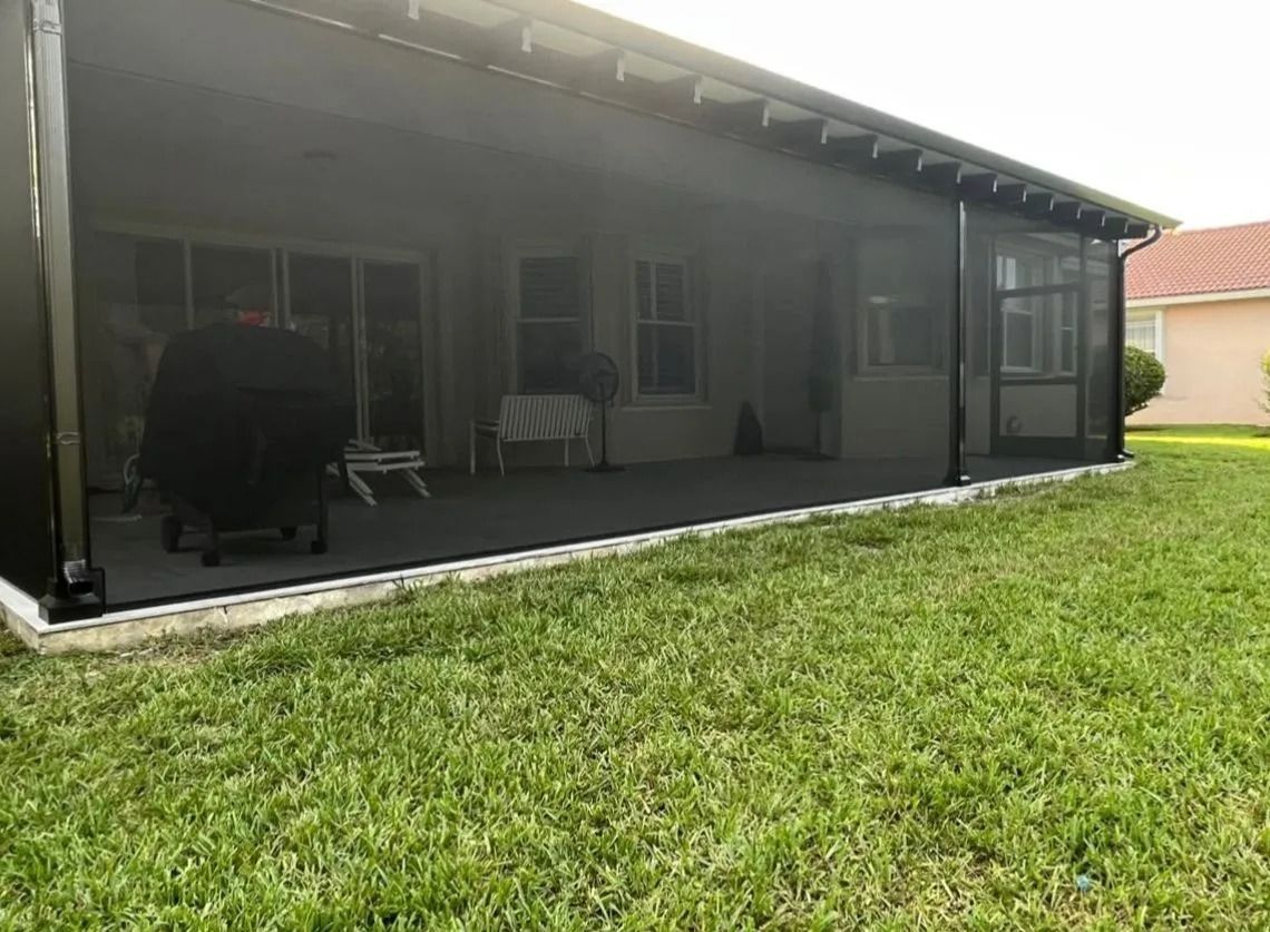 Screened porch with grill, overlooking a grassy yard. Black screening, gray flooring, and a white border.