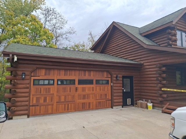 Brown log cabin with matching garage door and green roof under overcast sky.