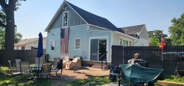 Backyard with a house, American flag, patio furniture, and a grill. Blue sky.