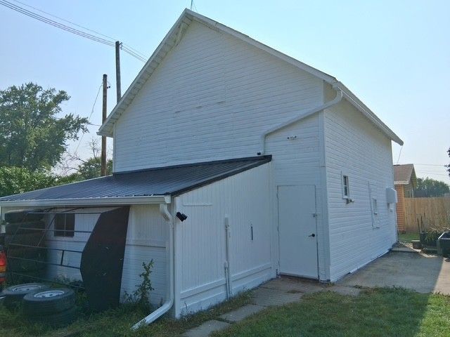 White two-story building with a shed attached, black roof, and a grassy area in front.