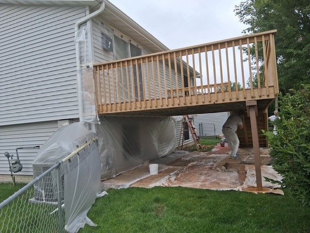 Deck being painted with enclosed underside. Person in white suit applies stain.