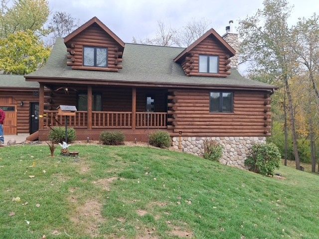 Log cabin with brown logs, green roof, and stone foundation on a grassy hill.