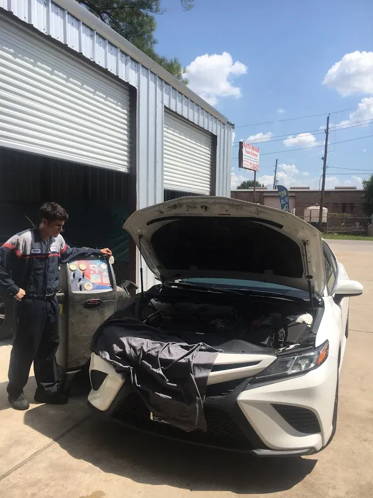 A man is standing next to a white car with the hood open.