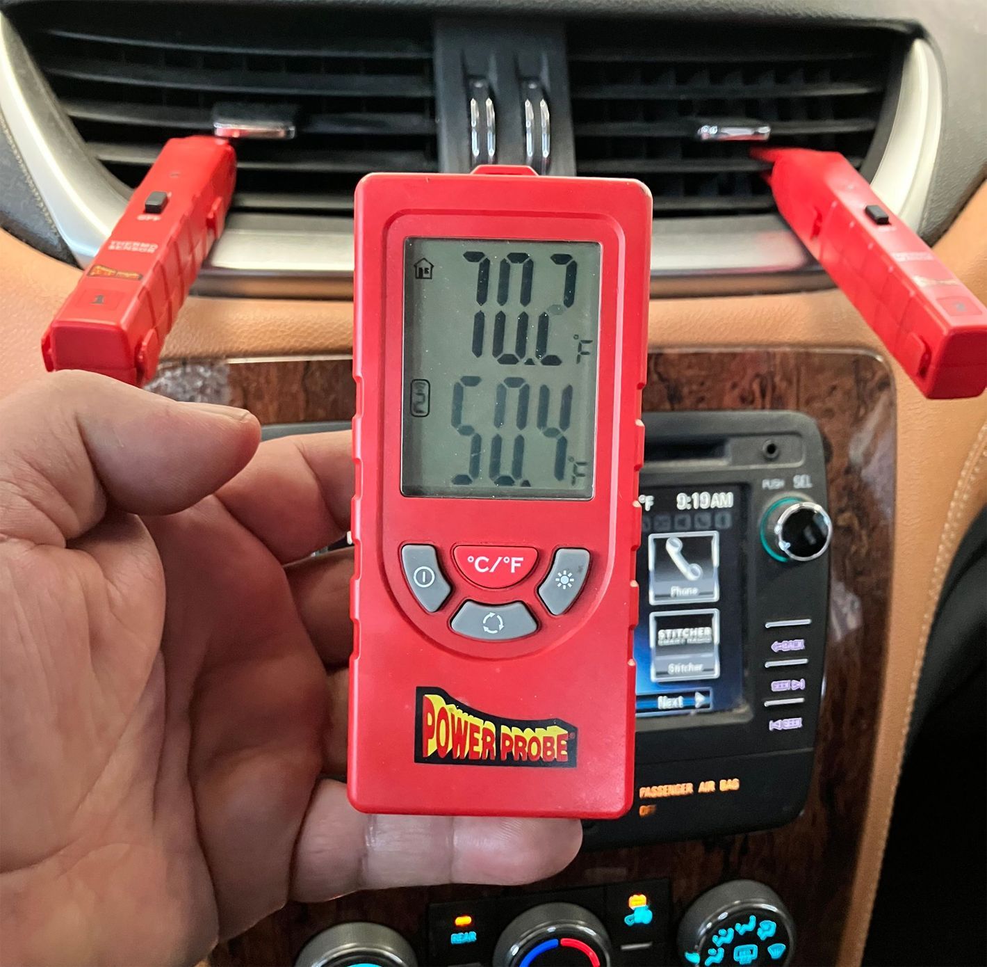 A hand holding a red tower proof thermometer in front of a car dashboard