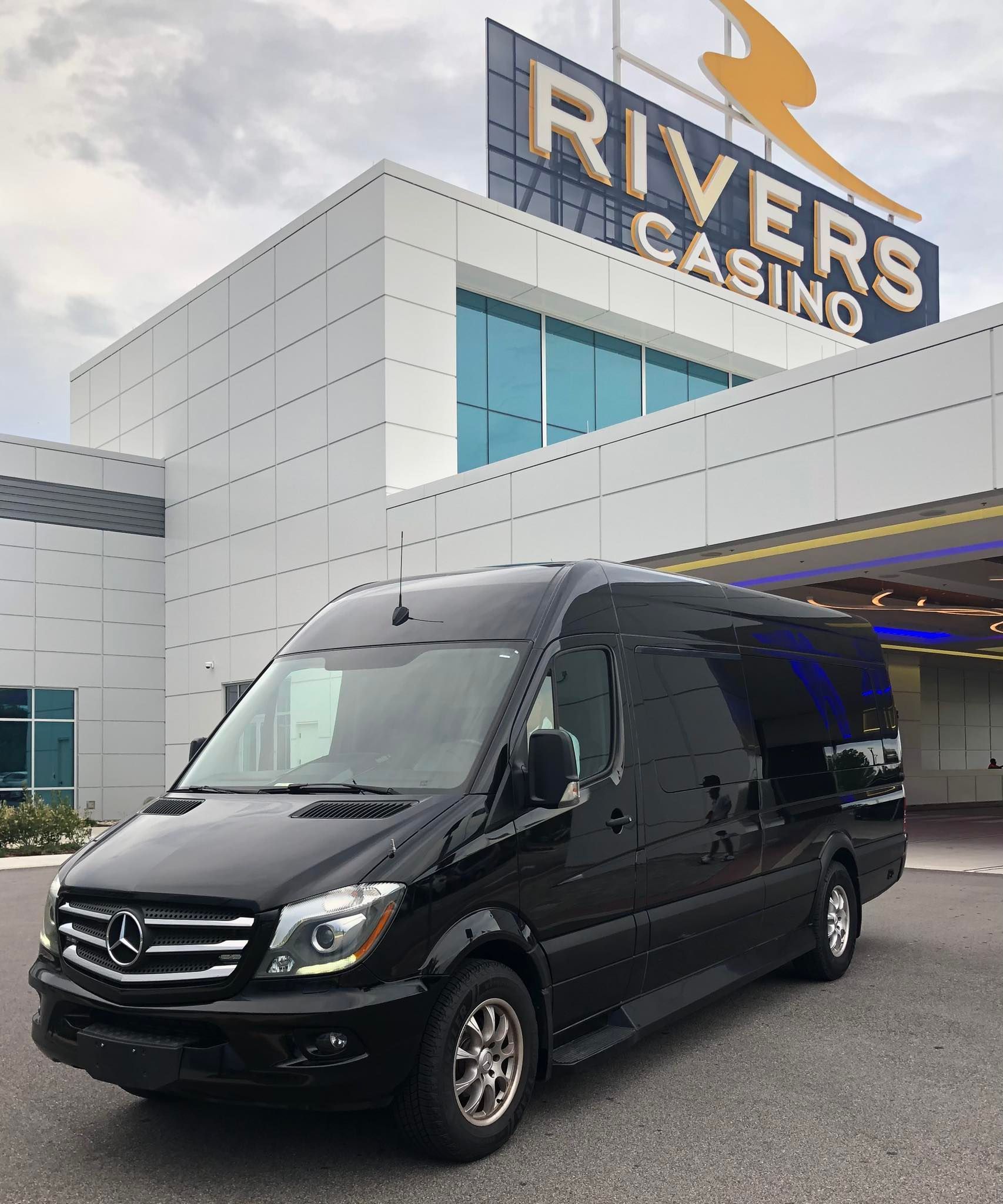 Black van parked in front of Rivers Casino. Building is white with blue windows and a sign.