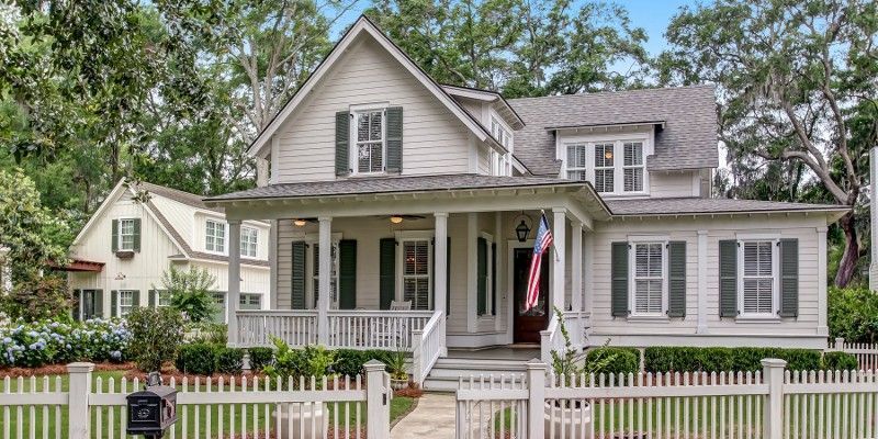 A white house with a large porch and a white picket fence.