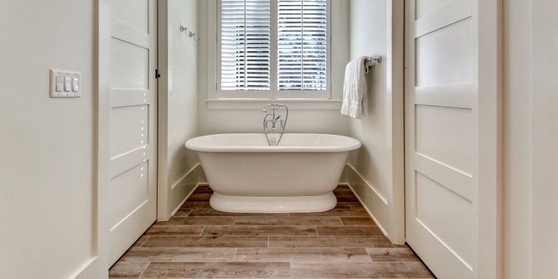 There is a bathtub in the middle of a bathroom between two doors.