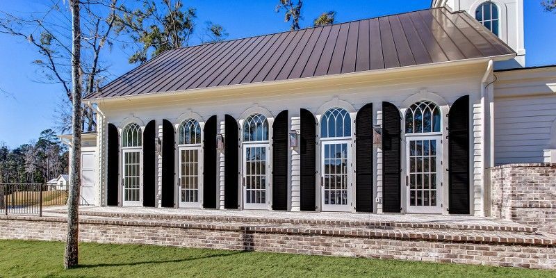 A white building with black shutters on the windows and a tree in front of it.