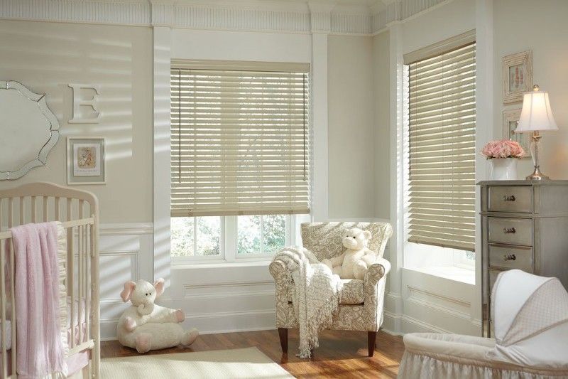 A nursery with a crib , chair , and window with blinds.