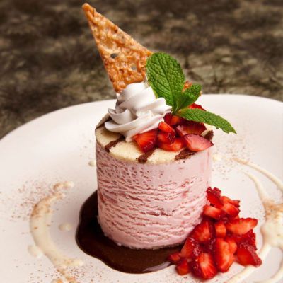 Pink strawberry dessert with whipped cream, fresh berries, mint, and a crisp wafer on a plate