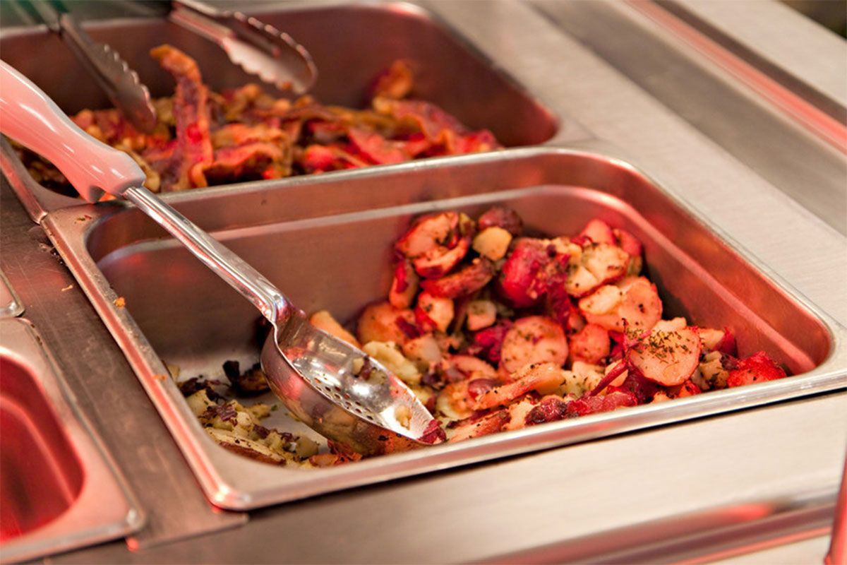 Tray of roasted vegetables being served with tongs at a buffet counter