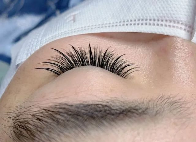 Close-up of a person's closed eye with long, dark, curled eyelashes. A white covering is near the eye.