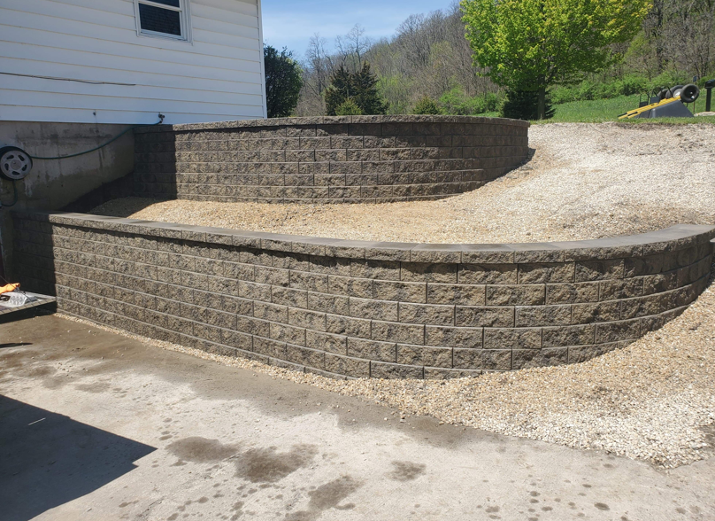 Tiered stone retaining walls beside a house, forming a landscaped driveway or patio area