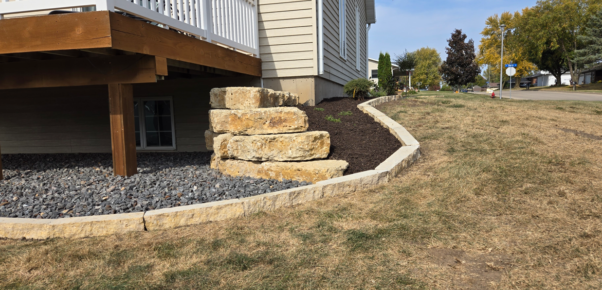 Stone steps beside a raised deck leading down to a grassy yard on a sunny day