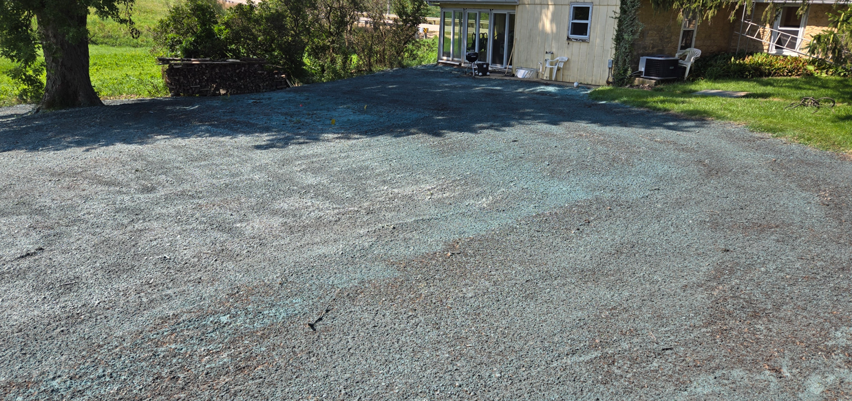 Blue gravel driveway leading to a house with trees and shrubs on either side