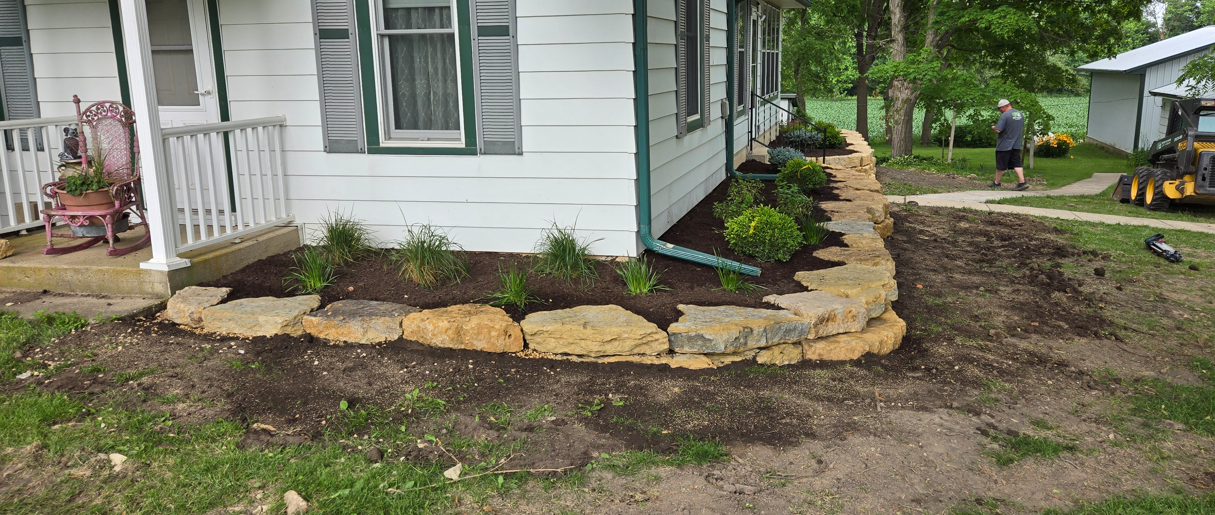 Fresh mulch and stone edging around a house foundation with a small landscaped garden bed