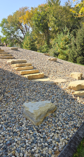 Stepped gravel path on a hillside with large rocks, bordered by autumn trees and blue sky