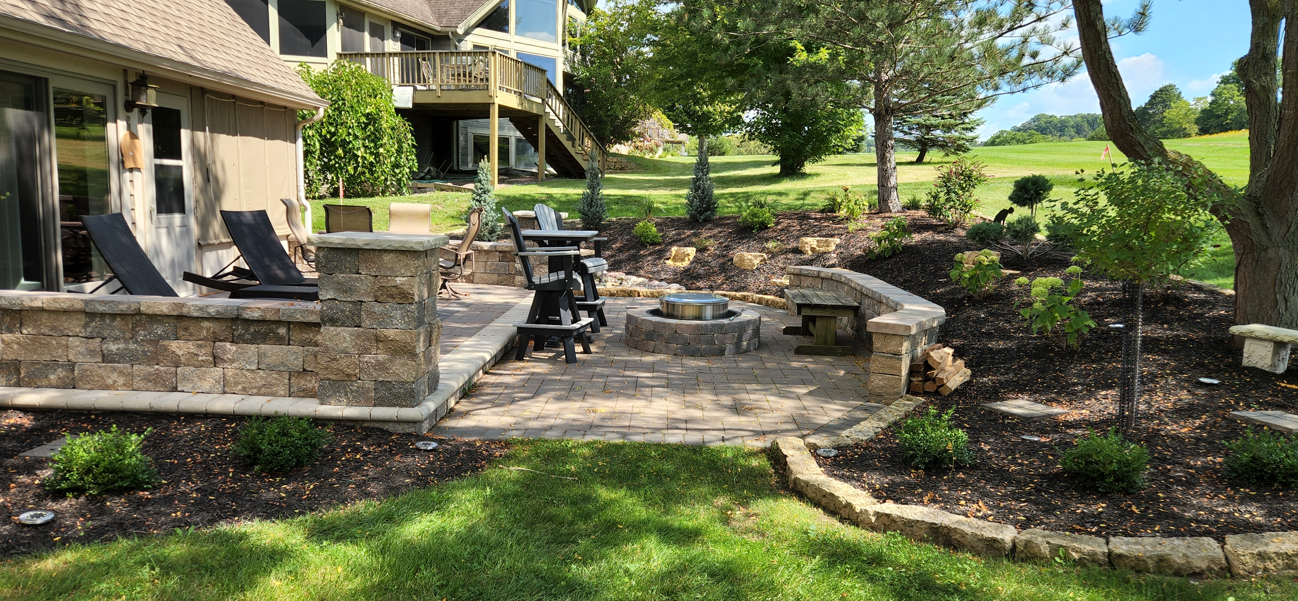 Backyard stone patio with outdoor furniture, grill, fire pit, and landscaped garden by a house