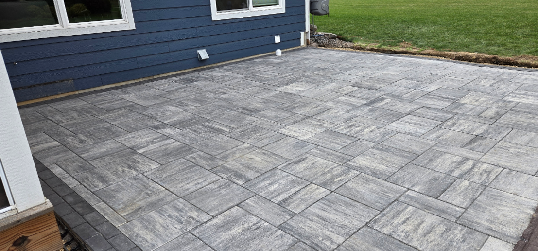 Gray stone patio beside a blue house and wooden fence