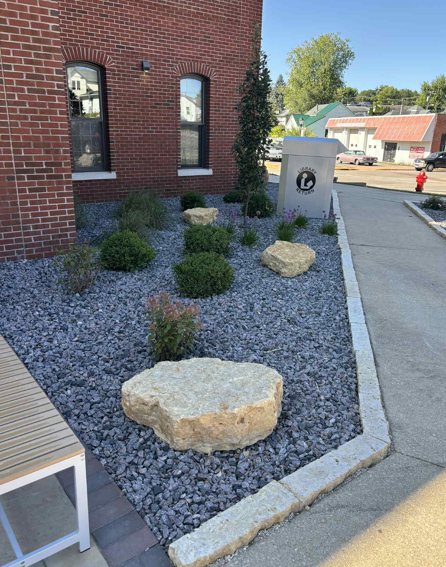 Brick building with a gravel rock garden, large boulders, shrubs, and a sidewalk beside it