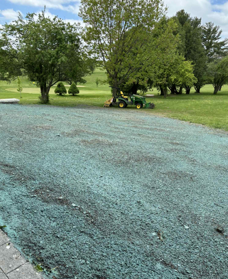 Gravel driveway beside a grassy yard with trees and a small green tractor in the distance
