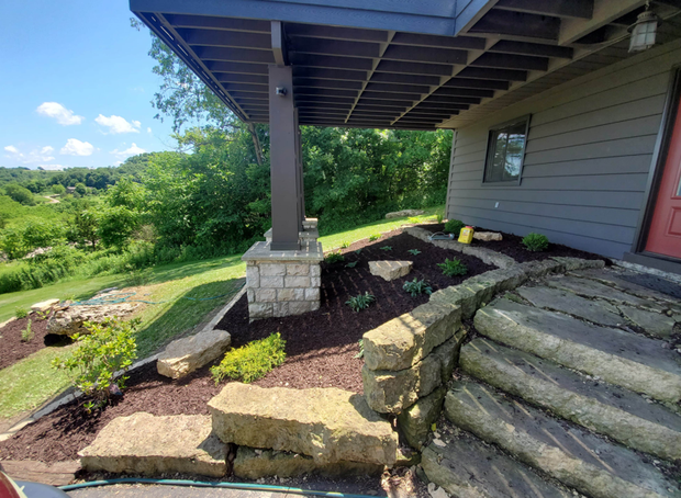 Stone steps and landscaped garden beside a house porch, with hillside view beyond.