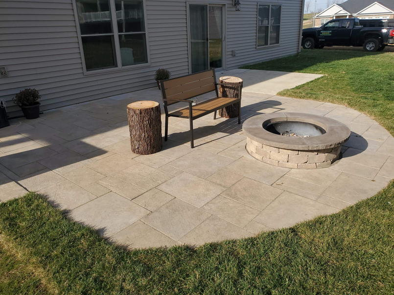 Backyard patio with a stone fire pit and wooden bench beside a house