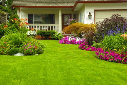 Lush front yard with bright flowers, green lawn, and a house porch in the background
