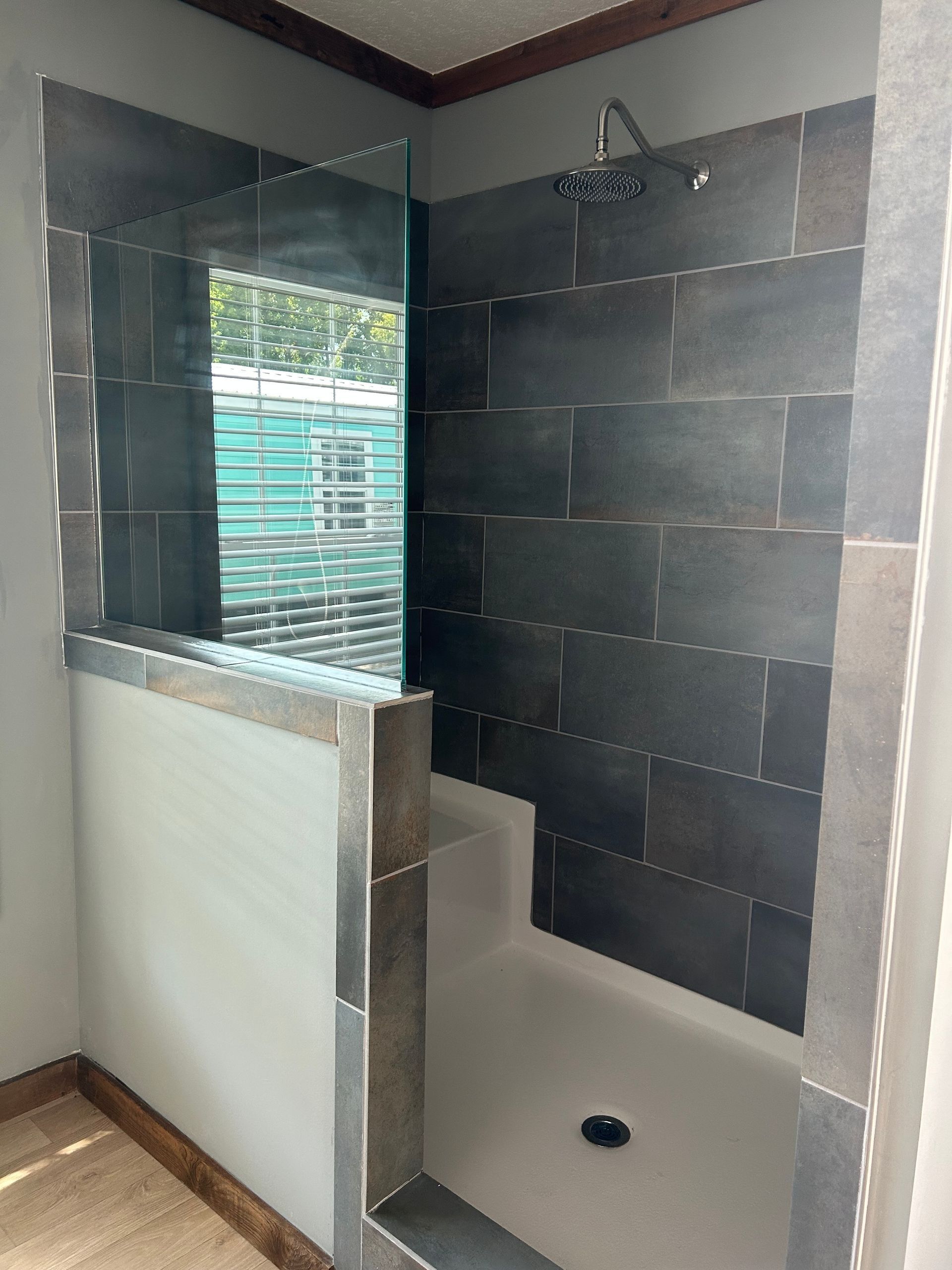 Walk-in shower with dark gray tiled walls, a glass partition, and a white base.