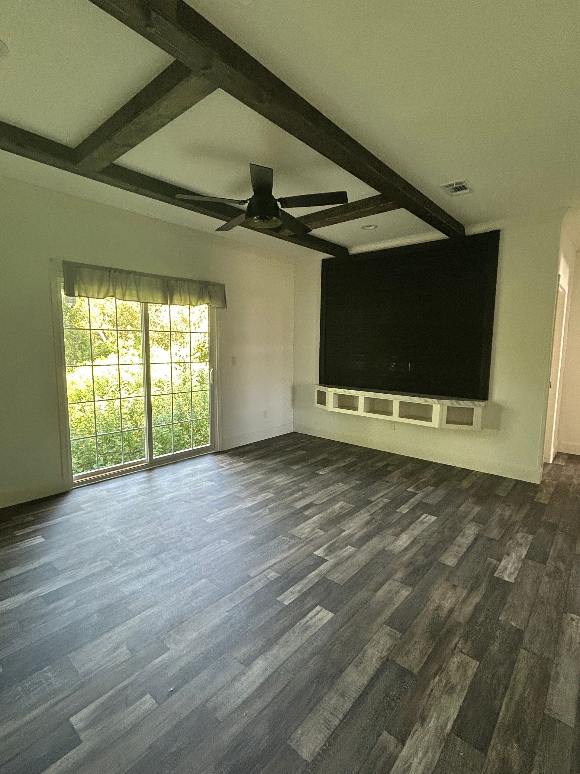 Empty living room with wood floors, exposed beams on the ceiling, black accent wall, and sliding glass doors.