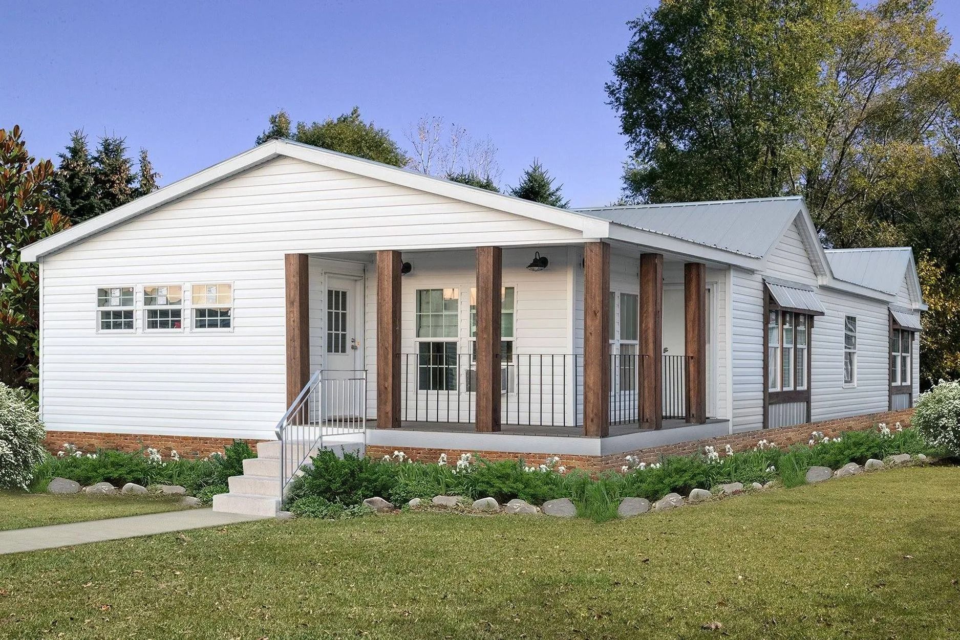 White house with porch and brown beams, set in a grassy yard with landscaping and trees.