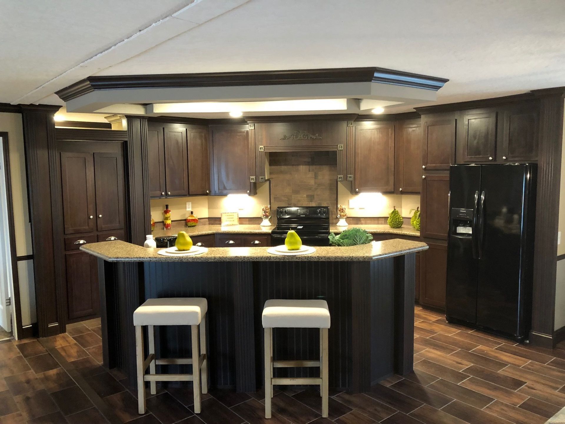 Kitchen with dark brown cabinets, island with stools, and black refrigerator.