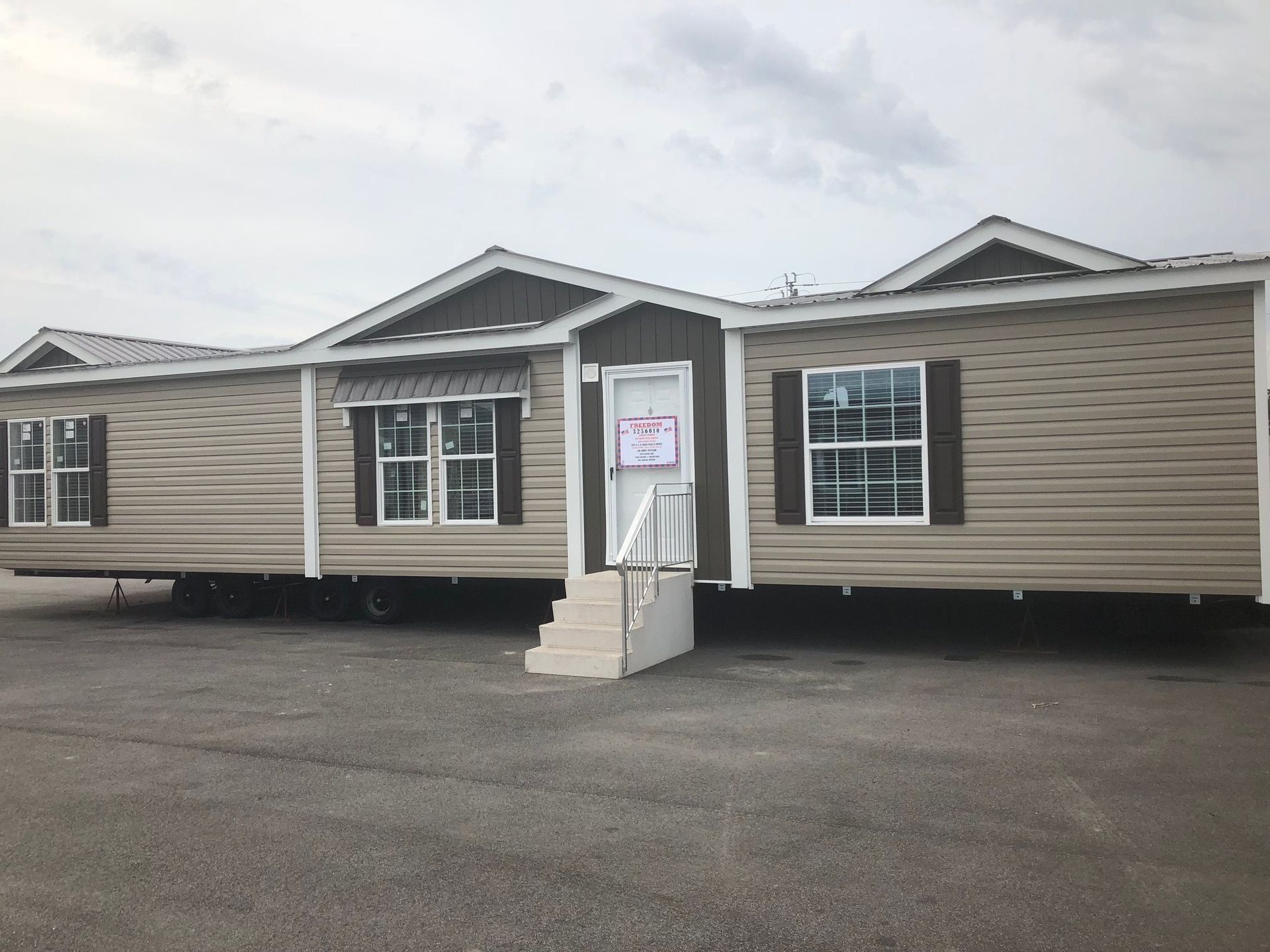 Tan manufactured home with brown trim, windows, and steps. Cloudy sky.