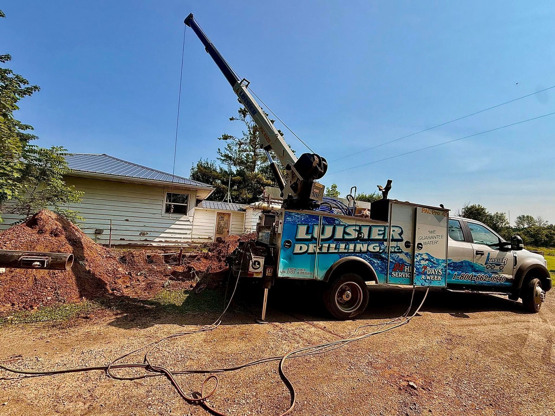 Truck-mounted crane lifting debris beside a house and dirt mound on a sunny day