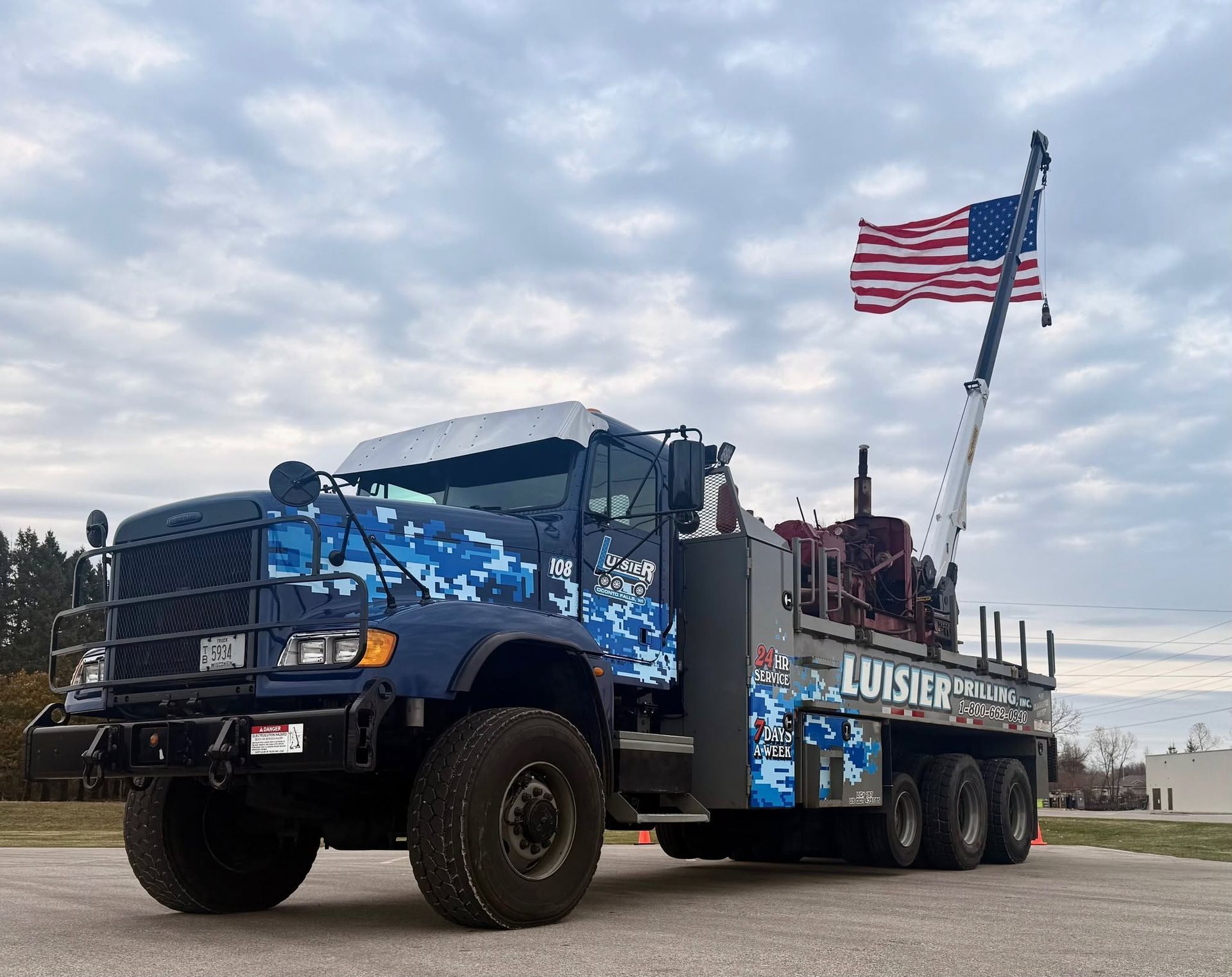 Blue lifted truck with American flag and crane in a lot.