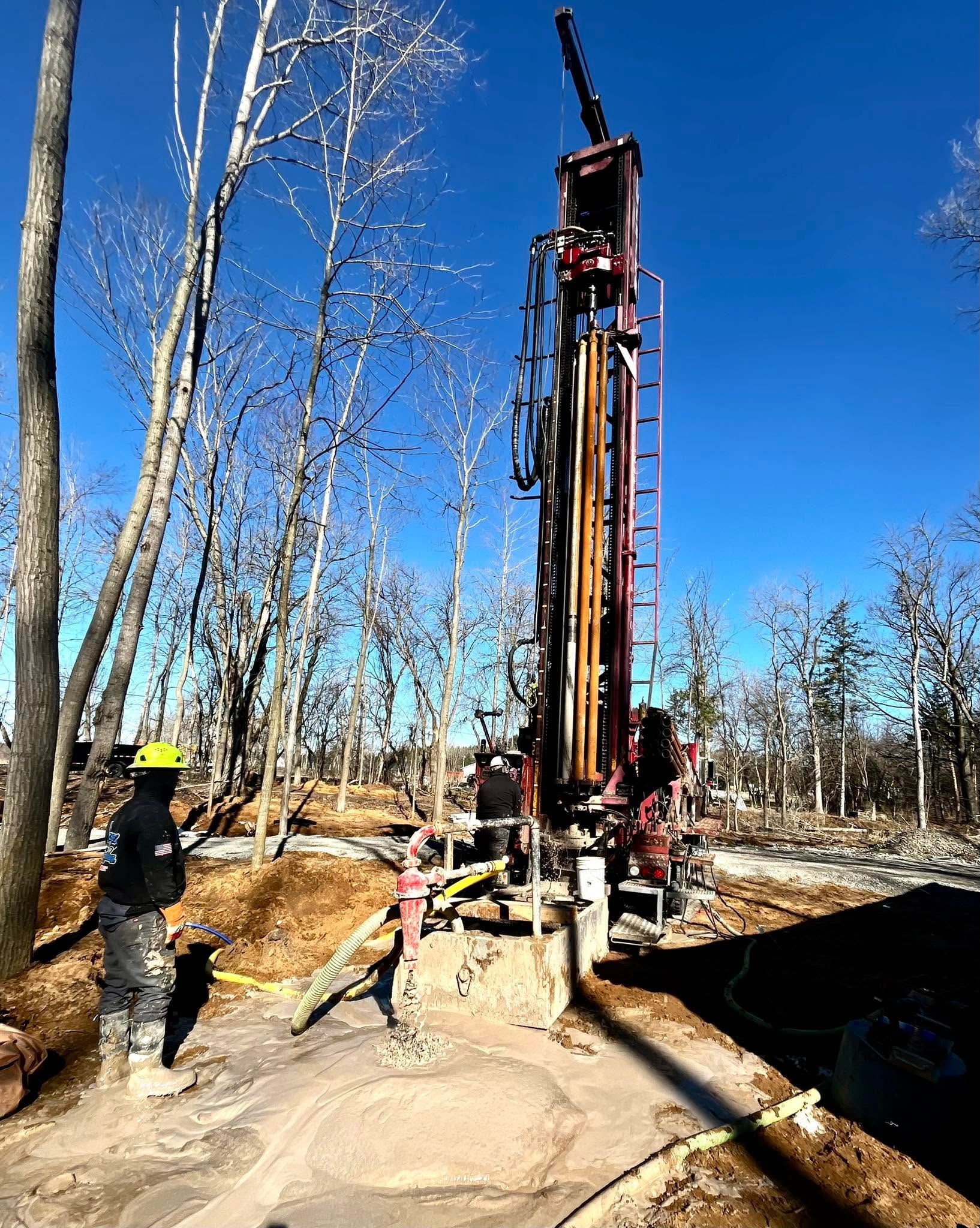 Drilling rig at a forest worksite with two people nearby under a clear blue sky