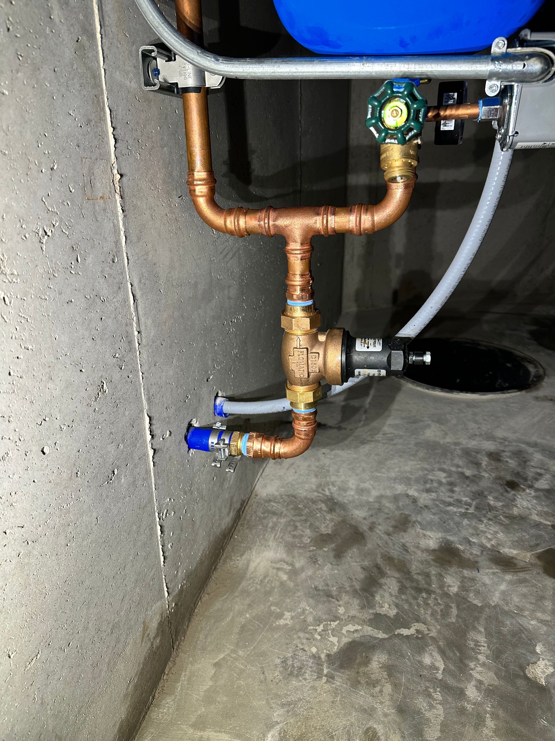 Copper plumbing pipes and valves beside a blue tank in a concrete utility area