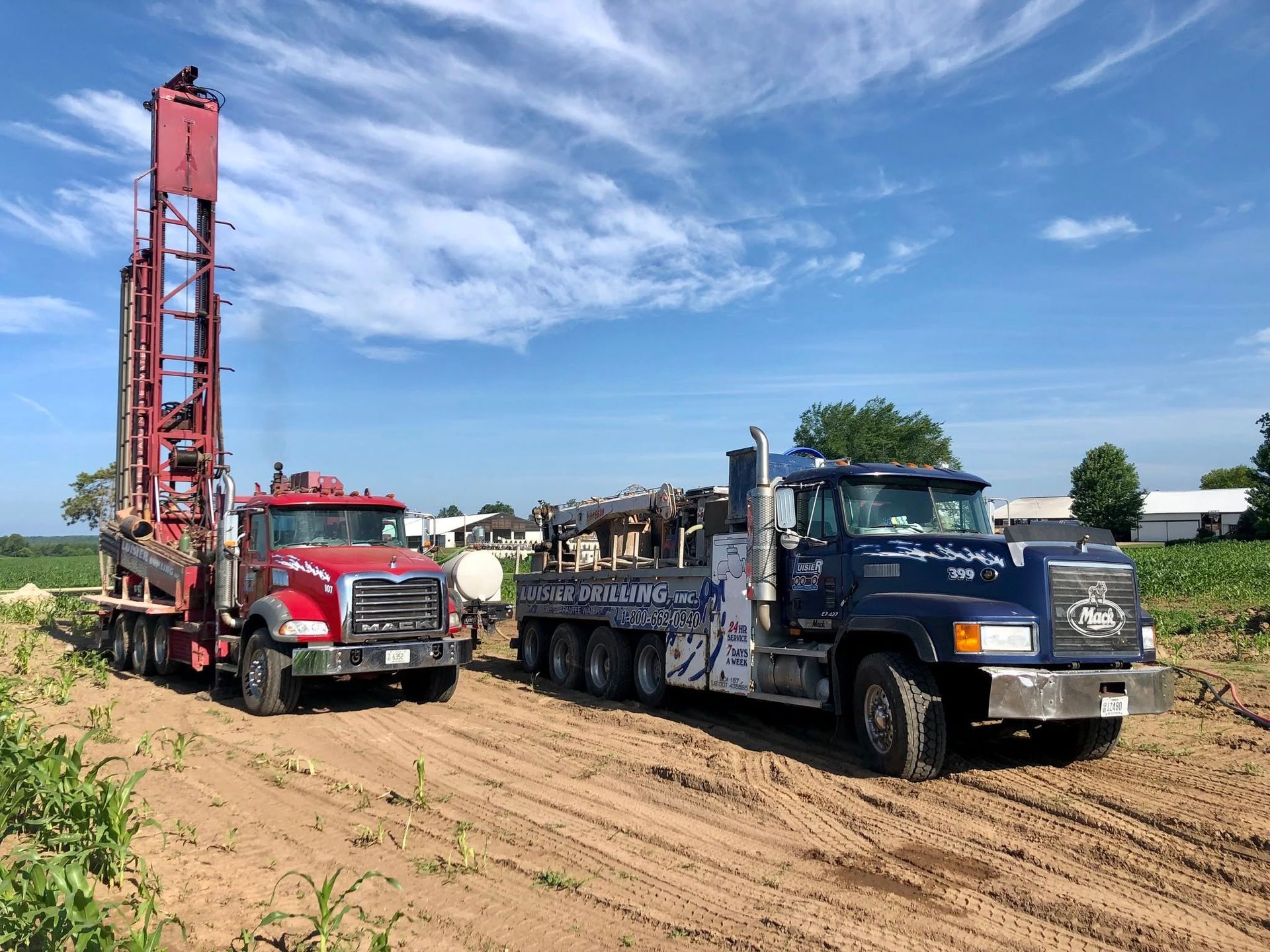 Two trucks and a tall red rig parked in a farm field under a blue sky.