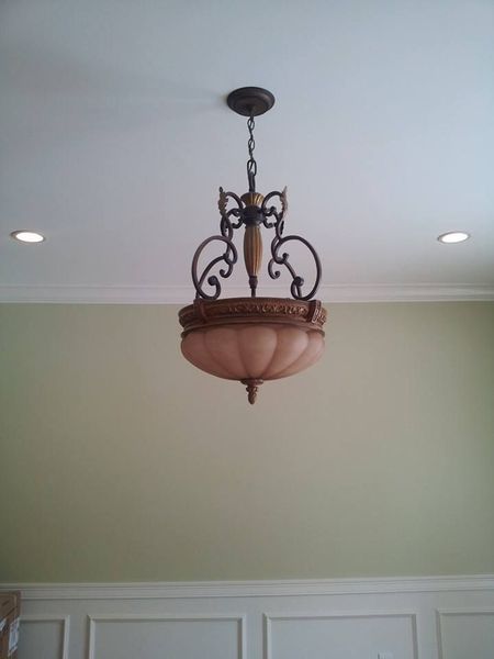 Chandelier hanging from a white ceiling over a light green wall, with two recessed lights.