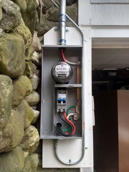 Exterior electrical meter box mounted on stone wall. Contains meter, circuit breaker, and wiring.
