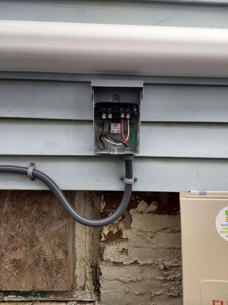 Electrical box mounted on a blue siding wall, with conduit running downwards.