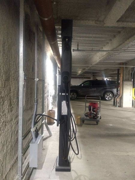 Electric vehicle charging station in an underground parking garage. Black charger, gray walls, car in background.