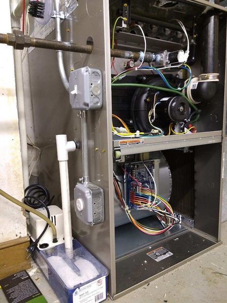 Furnace with open panels showing internal components, including wires, blower, and burners. Grey metal casing.