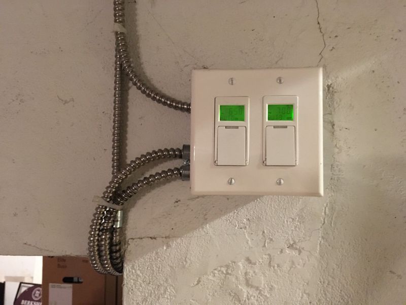 Two light switches with green indicators on a white wall, metal conduit nearby.