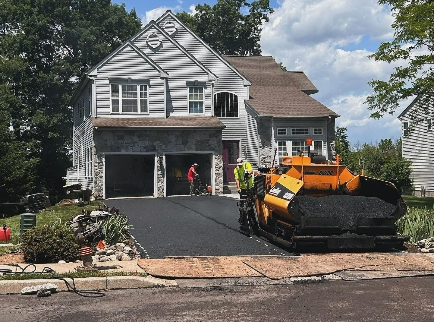 A construction worker operates yellow paving equipment to lay fresh asphalt on a residential driveway.