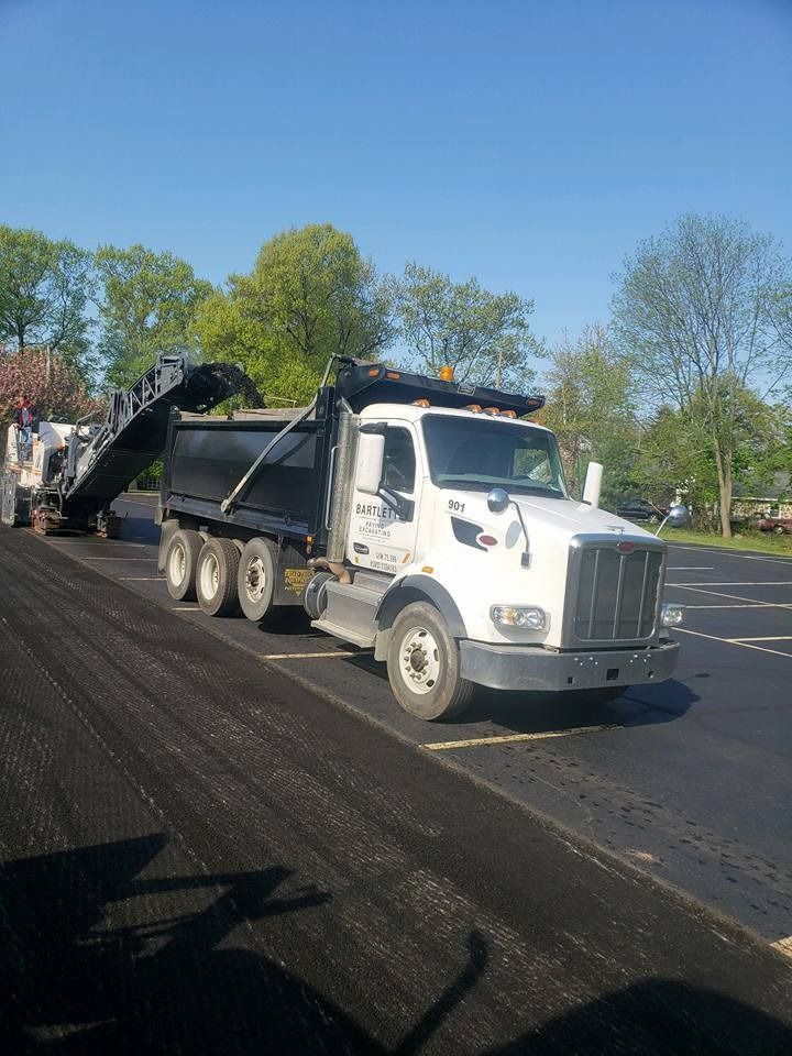 A white dump truck is positioned in an outdoor lot, being loaded with material by a heavy construction machine.