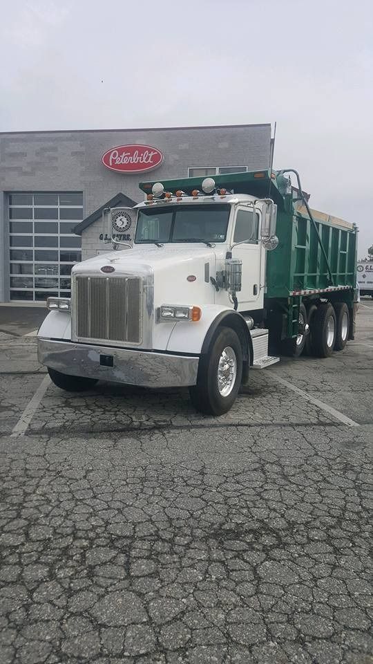 A white Peterbilt dump truck with a green bed parked in a lot in front of a Peterbilt dealership.