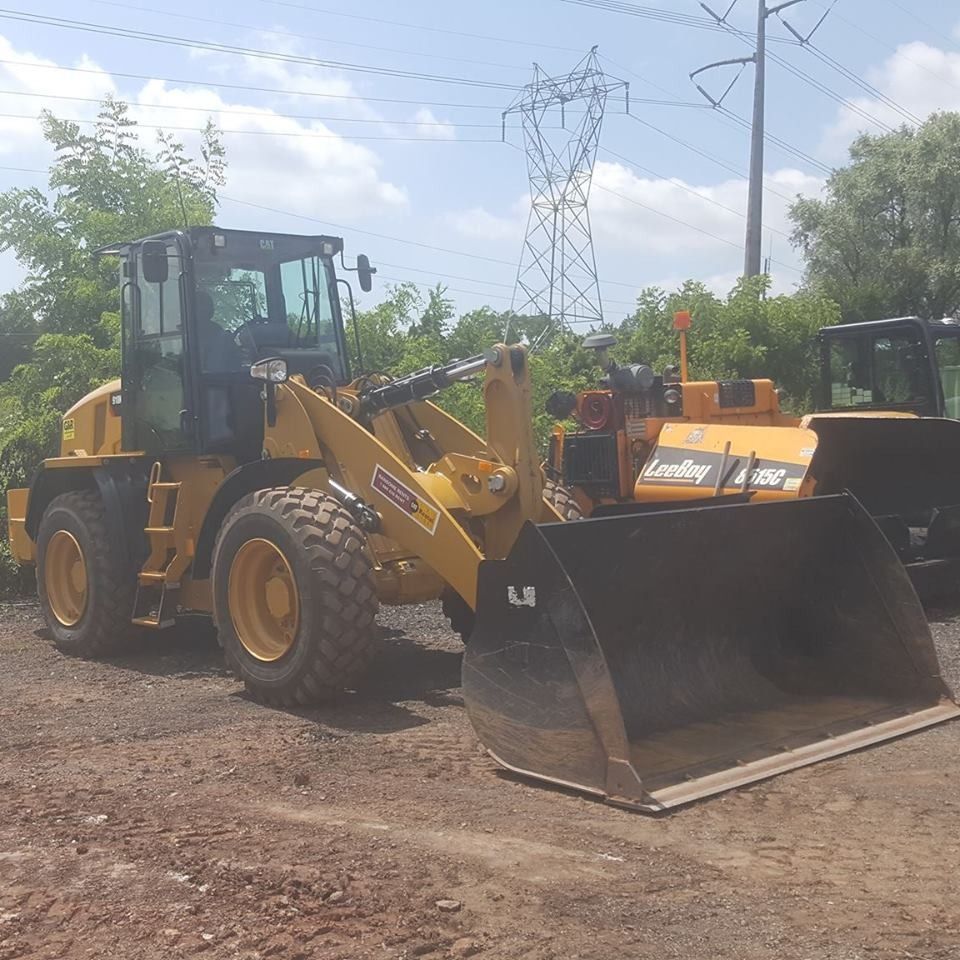 A yellow Caterpillar wheel loader parked on a dirt lot with an industrial power line tower in the background.